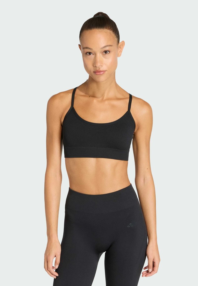 Μαύρο αθλητικό σουτιέν με λεπτές τιράντες, φαρδιά ζώνη και λείο υλικό; συνδυά�ζεται με ψηλόμεσα μαύρα κολάν που διαθέτουν μια διακριτική επωνυμία.