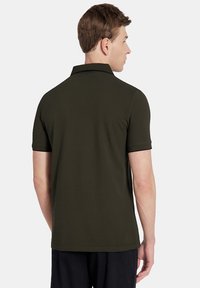 Oliwkowa koszulka polo z krótkim rękawem, płaskim kołnierzykiem i czarnymi wykończeniami. Gładka bawełniana tekstura, dół koszulki sięga na wysokości bioder.