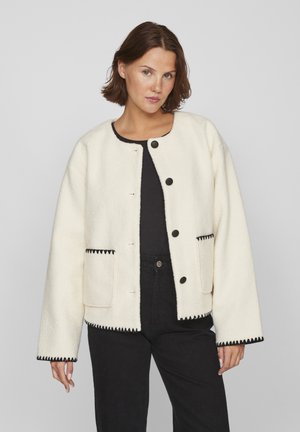 Veste blanche texturée avec des finitions noires, dotée d'un col rond, de poches avant et de boutons noirs. Design simple avec une coupe décontractée.
