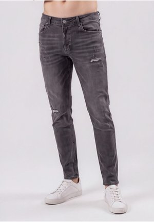 Slank pasform falmet sort jeans med slidte detaljer båret med hvide sneakers på en stående mandlig model.