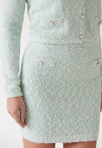 Mintgroene, gestructureerde jas en rokset van boucle-stof, met parel-accenten op de zakken en een getailleerd silhouet.