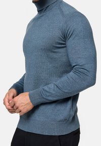 Pull bleu à col roulé en maille côtelée. Présente des manches longues, une coupe ajustée et un petit logo près de l'ourlet.