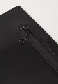 Schwarze Lackledertasche mit einem Reißverschluss. Ausgestattet mit einem YKK-Reißverschlusszipp und glatter, glänzender Oberfläche. Saubere Kanten und minimalistisches Design.