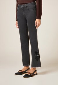 Jeans in denim grigio con orlo sfrangiato e dettaglio di ricamo floreale nero sulla parte inferiore della gamba, abbinati a ballerine nere con punta e accento a righe.