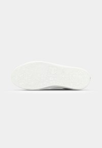 Suela de zapatilla blanca con un patrón de agarre texturizado y un detalle de logotipo central. La goma tiene surcos sutiles que mejoran la tracción.