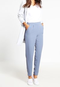 Ljusblå skräddarsydda byxor med sidofickor, subtila veck och smal passform, kombinerat med en vit t-shirt och en ljus kavaj.