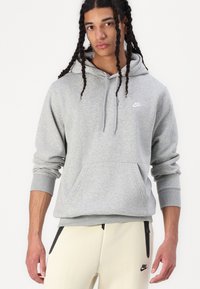 Camisola com capuz cinzenta com um bolso frontal, punhos e bainha canelados; apresenta um pequeno logotipo branco da Nike no peito. Textura do tecido lisa.