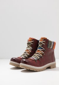 Botas de cuero rojo con acentos de punto multicolor, punta redonda, suela de goma beige y cordones en contraste con ojales de metal.