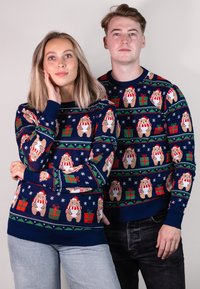 Ein Paar blauer Weihnachts-Pullover mit Bärendesigns, die Weihnachtsmannmützen, rote Schals und Geschenk-Motive tragen. Strickmaterial mit gerippten Bündchen.