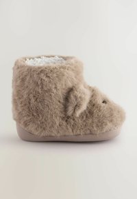 Flauschiger beiger Hausschuh mit weicher Textur, runder Form und weißem Innenfutter. Besitzt einen kleinen Akzent an der Vorderseite und eine flache Sohle.