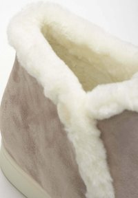 Suède pantoffel in zacht beige met een fluffy crèmekleurige bontvoering en -buis, voorzien van een afgeronde kraag en een soepele, gebogen silhouet.