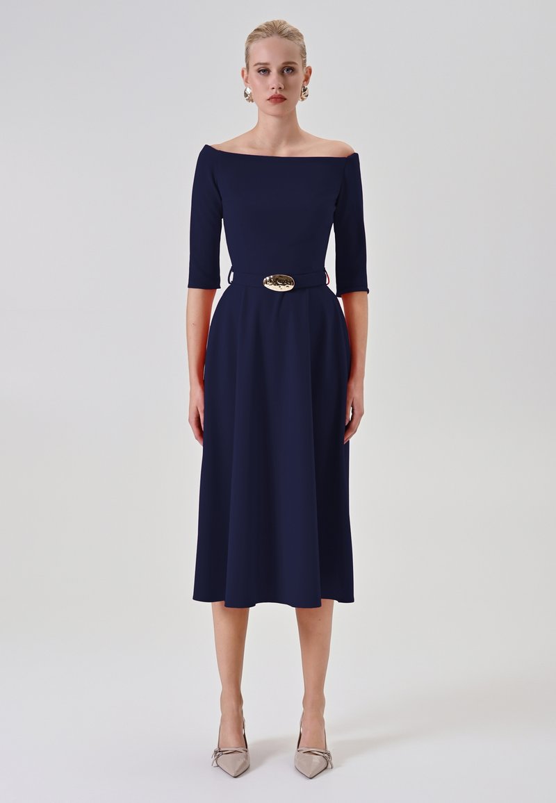 Navy Off-Shoulder Kleid mit Dreiviertelärmeln und taillierter Passform, mit einem goldenen Schnallen-Gürtel. Elegante A-Linie und glattes Material.