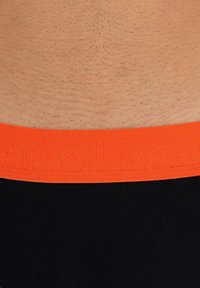 Musta kangaskalvot orange elastisella vyötärölinjalla, jossa on kohokuvioitu teksti. Tasainen pinta, muotoiltu malli ja vähäiset ompelusaumat.