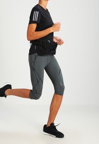 Czarna koszulka krótki rękaw z trzema białymi paskami, szare legginsy capri w wzory oraz czarne buty do biegania. Torebka na pasek noszona w talii.