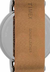 Montre Timex avec un boîtier rond en acier inoxydable argenté, un bracelet en cuir véritable marron au toucher texturé et une résistance à l'eau allant jusqu'à 50 mètres.