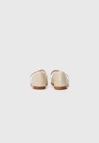 Chaussures en cuir à enfiler crème avec une texture lisse, un talon bas et des liens ajustables à l'arrière pour un maintien sécurisé.