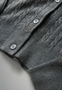 Grauer Kabelstrick-Cardigan mit gerippten Bündchen und Saum, der transparente runde Knöpfe entlang der Vorderseite hat.