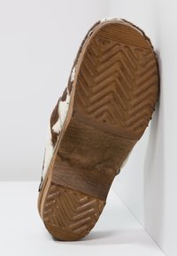 Bruine en witte geprinte schoenonderkant met een geprofileerde rubberen zool, voorzien van een visgraatpatroon en zichtbare stiksels.