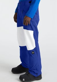 Blue snow pants with large white accents, zippered pockets, and adjustable cuffs, made from a waterproof material. Black logo tag visible.