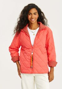 Kurteczka z pikowanej koralowej tkaniny z kontrastowym brązowym kołnierzem, zamkiem błyskawicznym z przodu oraz kolorowym uchwytem zamka. Posiada rękawy o średniej długości.