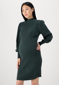 Robe tricotée côtelée de couleur vert foncé, avec un col haut et des manches bouffantes, silhouette ajustée, texture douce et longueur à mi-genoux.