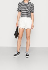 Top a maniche puff a scacchi bianco e nero abbinato a pantaloni shorts in denim bianco strappati e sneakers nere, mentre tiene una borsa nera testurizzata.