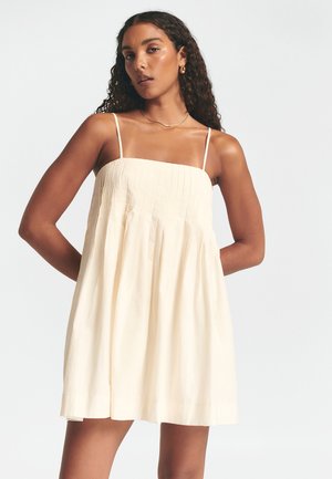 Lyscreme ærmeløs kjole med firkantet udskæring, plisseret stoftekstur og A-formet silhuet, der når til midt på låret.