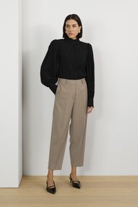 Blouse noire à rayures avec des manches bouffantes, assortie à un pantalon beige à rayures. Complétée par des chaussures à talons noires. Design minimaliste.