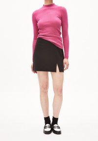Fitted rosa ribbad polotröja i kombination med en svart mini-kjol med en sidslits, kompletterad med svarta strumpor och loafers.