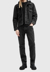 Giacca di jeans nera e jeans abbinati a un cappuccio nero, con due tasche sul petto e una texture liscia. Completato con stivali neri.