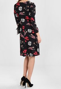 Czarna sukienka w kwiaty z długimi rękawami, dopasowanym krojem i długością do kolan. Użyta w niej kolorowa florystyka w odcieniach czerwieni i bieli.