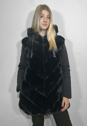 Gilet in pelliccia sintetica nera con motivo a zigzag, chiusura con zip e cappuccio. Presenta maniche in tessuto nero e una texture liscia.