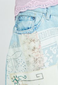 Denim shorts met een patchwork ontwerp van bloempatronen en kant in zachte pastelkleuren, gecombineerd met ruwere denimtexturen.