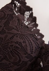 Gros plan sur un tissu en dentelle noire à motifs floraux et bords festonnés sur un vêtement.