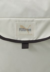 Sac Puma en tissu gris clair avec accents noirs, arborant une étiquette logo cousue indiquant « IL N'Y A QU'UN SEUL POUR TOUJOURS. »