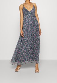 Maxi-jurk in donkere bloemendruppel met dunne bandjes, geplooide buste, vloeiende silhouette en gelaagde textuur met groen- en paars tinten.