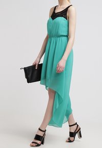 Bezramenné tyrkysové šaty s černým krajkovým korzetem, splývavým lemem a zúženým pasem. V kombinaci s černými lodičkami a psaníčkem.