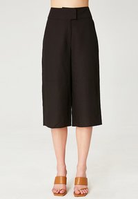 Culottes noires à jambes larges avec une taille haute, présentant une texture lisse et un design soigné. Accompagnées de sandales à glissière beiges.