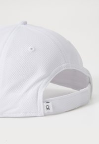 Fehér baseball sapka hálós anyagból. Hátsó részén állítható pánttal rendelkezik, valamint egy kis látható címkével, amelyen a "CK" logó látható.