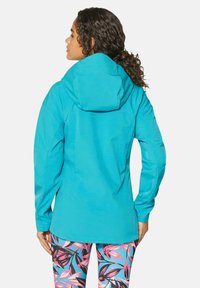Türkisfarbene wasserdichte Jacke mit Kapuze, langen Ärmeln und lockerer Passform, kombiniert mit lebhaften leggings im Blättermuster.
