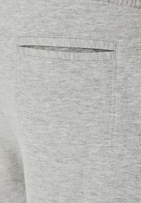 Jasnoszare dresy mają delikatną teksturę oraz jedną tylnią kieszeń z poziomym otwarciem, przeszycia i elastyczny pas.