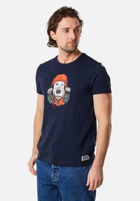 Navyblaues Baumwoll-T-Shirt mit einem Grafikmotiv eines Hundes in einem orangefarbenen Hut, verziert mit grünen Kopfhörern. Klassischer Rundhalsauschnitt und lockere Passform.