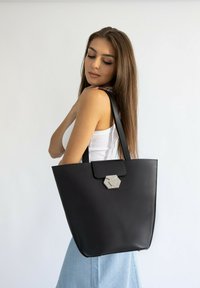 Borsa tote nera in pelle liscia con una chiusura esagonale in argento e spalline piatte, caratterizzata da un design minimalista e una forma verticale.