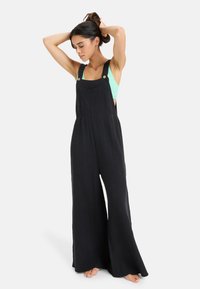 Pantalones de tirantes negros de pierna ancha hechos de una tela texturizada, con tirantes ajustables, detalles de botones y un ajuste holgado para mayor comodidad.