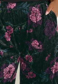 Blommiga sammetspants med en mörkgrön bas och rosa och lila blommor samt blad, med en rynkad midja och sidofickor.