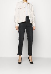 Ljusbeige denimjacka med två bröstfickor, bärs över en vit topp, matchad med högmidjade svarta jeans och svarta högklackade skor.