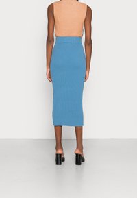 Žebrovaná pletená modrá midi sukně s vysokým pasem a těsným střihem, spárovaná s lehkým hnědým topem bez rukávů a černými sandály na blokovém podpatku.