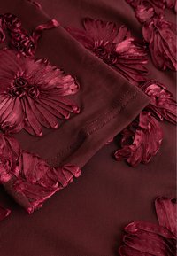 Burgundia kangas, millel on reljeefne lilleline tikand erinevates punaste toonides. Kujunduses on tekstuuriga õielehed ja ringjad lillekeskmed.