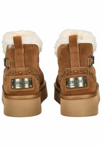 Bruine suède enkelboots hebben een fuzzy, crèmekleurige kraag, decoratieve studs en een metalen merkteken op de hak. Platte rubberen zool.