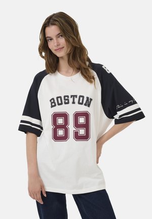 Baltas ir tamsiai mėlynas per didelis marškinėliai su "BOSTON" juoda spalva ir "89" bordo. Marškiniai turi juostuotas tamsiai mėlynas rankoves ir rašytinį detalų ant rankovės.